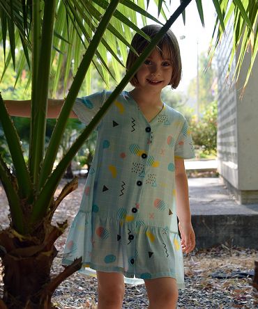 Vestido infantil geométrico, de manga corta, hecho en viscosa, con estampado de cuadrícula y motivos geométricos sobre fondo celeste.