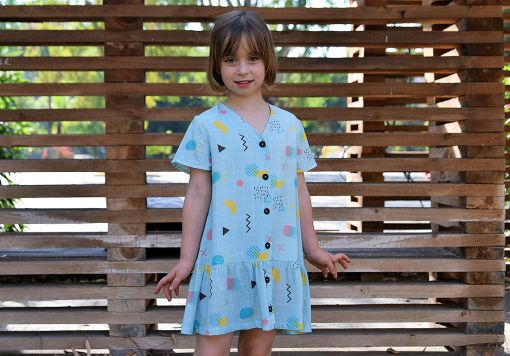 Vestido infantil geométrico, de manga corta, hecho en viscosa, con estampado de cuadrícula y motivos geométricos sobre fondo celeste.