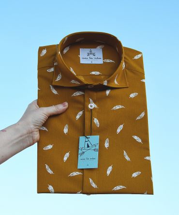 Camisa estampada de hombre, de manga corta, hecha en algodón orgánico, con estampado de plumas sobre fondo mostaza. Hecha en España de manera sostenible.