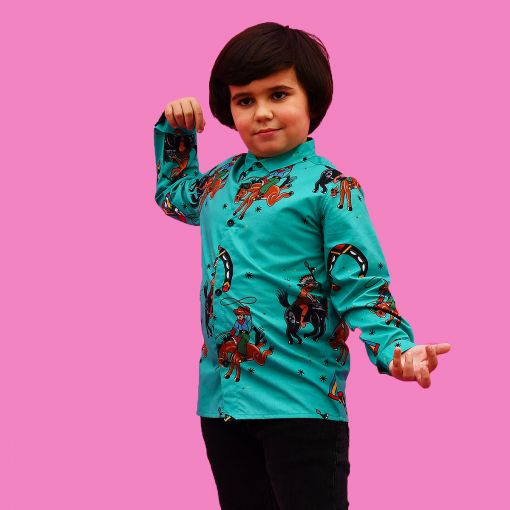 Camisa de niño estampada con indios y vaqueros sobre fondo turquesa. Es de manga larga y está hecha en algodón orgánico, de manera sostenible