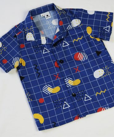 Camisa de niño estampado geométrico sobre fondo azul. Es de manga corta y está hecha en algodón orgánico, de manera sostenible.